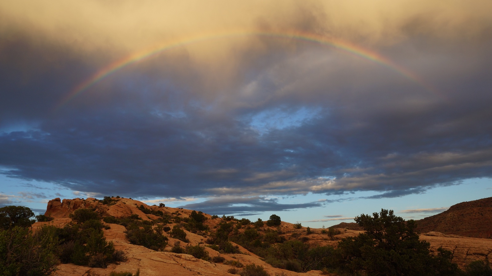 A rainbow arches across dark clouds above rocky terrain.